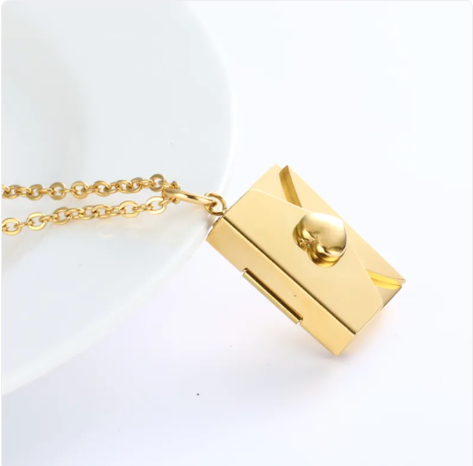 Gold envelope locket necklace with heart clasp, angled view on a white dish