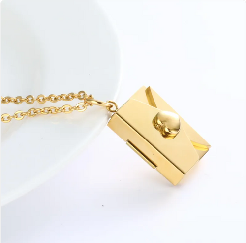 Gold envelope locket necklace with heart clasp, angled view on a white dish