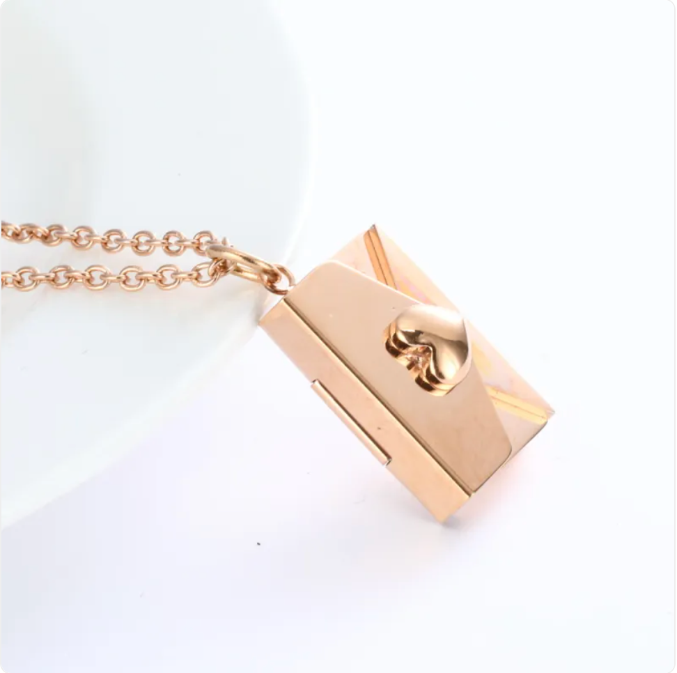 Rose gold envelope locket necklace, angled view on a white dish